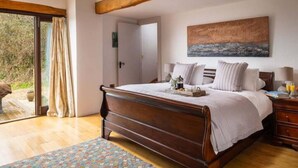 A bedroom with a wooden bed, a painting on the wall, and a view through the window. - Retreat With Valley-view Deck (Ilfracombe)