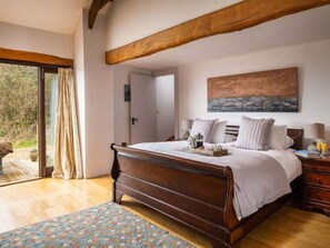 Ein Schlafzimmer mit einem hölzernen Bett, einem Gemälde an der Wand und Blick durch das Fenster.