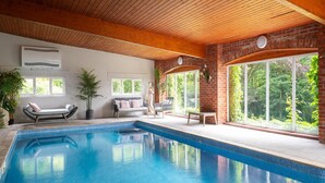 An indoor swimming pool with a wooden ceiling, a brick wall, and large windows offering a view of greenery. - Retreat With Valley-view Deck (Ilfracombe)