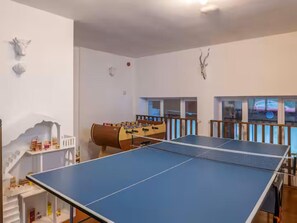 Una habitación con mesa de ping pong, mesa de fútbol de mesa y ventana con vista al exterior.