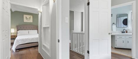 A hallway leading to a bedroom with a bed, a nightstand, and a wall-mounted light fixture.