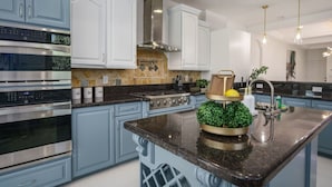 A modern kitchen with stainless steel appliances, light blue cabinetry, and a central island with a decorative plant. - Riverfront Estate | Pool, Dock & Game Room (Palm City)
