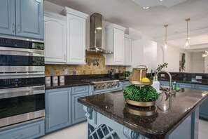 A modern kitchen with stainless steel appliances, light blue cabinetry, and a central island with a decorative plant. - Riverfront Estate | Pool, Dock & Game Room (Palm City)