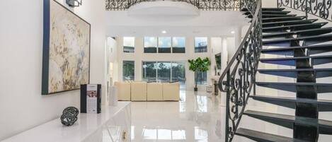 Interior espaçoso com escadaria moderna, uma grande pintura abstrata e um espaço de estar minimalista.
