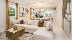 A modern living room with a sectional sofa, a coffee table, and a dining area with a chandelier. - Riverfront Estate | Pool, Dock & Game Room (Palm City)