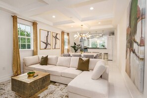 A modern living room with a sectional sofa, a coffee table, and a dining area with a chandelier. - Riverfront Estate | Pool, Dock & Game Room (Palm City)