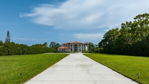 A large building with a central entrance, surrounded by a well-maintained lawn and trees. - Riverfront Estate | Pool, Dock & Game Room (Palm City)