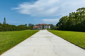 A large building with a central entrance, surrounded by a well-maintained lawn and trees. - Riverfront Estate | Pool, Dock & Game Room (Palm City)