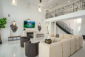 Un salón amplio con un sofá grande, una chimenea, un televisor y una escalera.