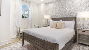 A bedroom with a bed, two bedside tables with lamps, a window with curtains, and a ceiling fan. - Riverfront Estate | Pool, Dock & Game Room (Palm City)