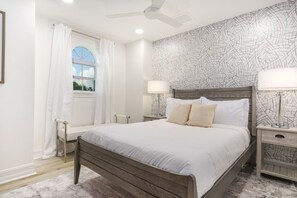A bedroom with a bed, two bedside tables with lamps, a window with curtains, and a ceiling fan. - Riverfront Estate | Pool, Dock & Game Room (Palm City)