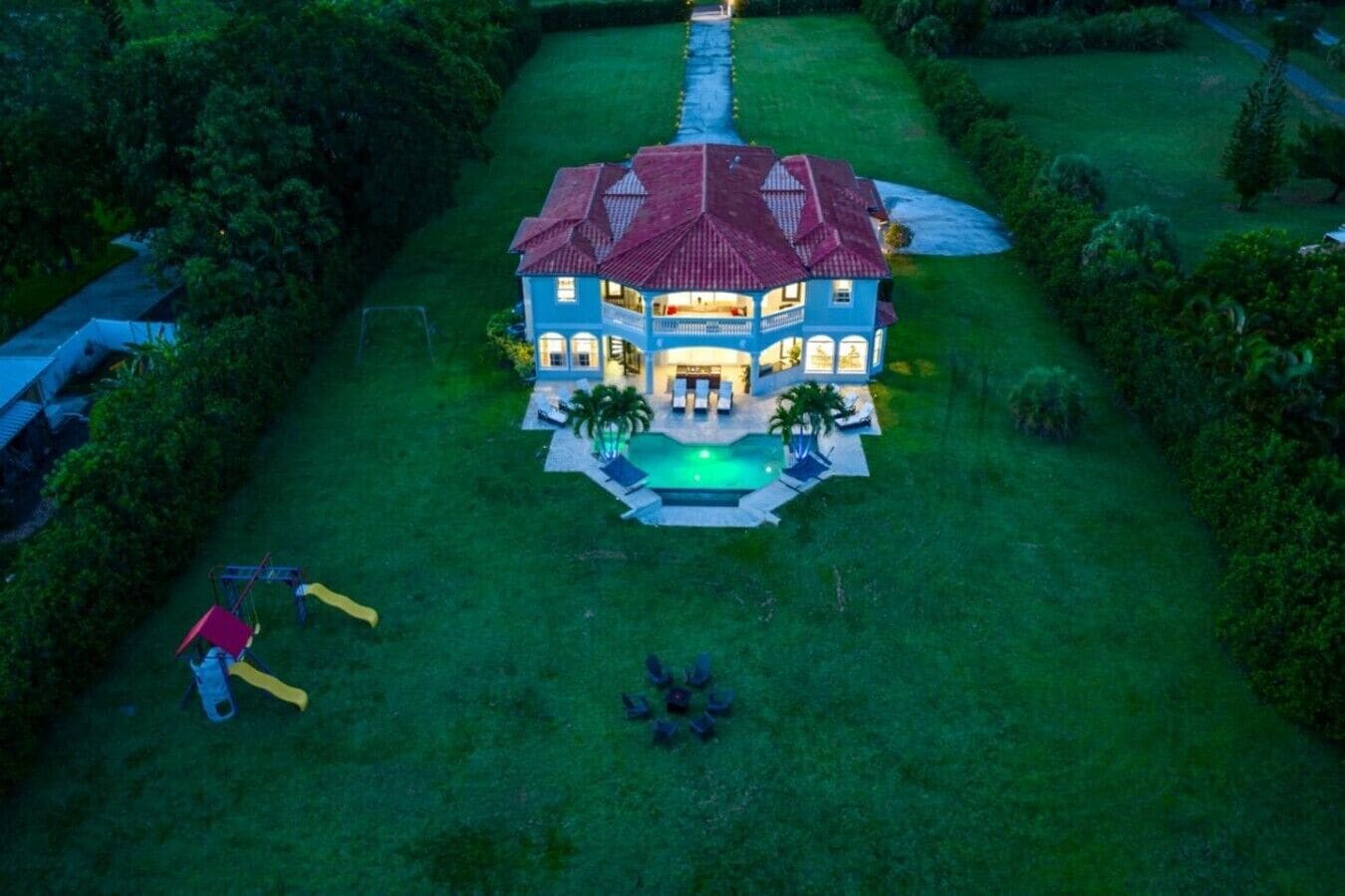 A large house with a swimming pool, surrounded by a well-maintained lawn and trees.