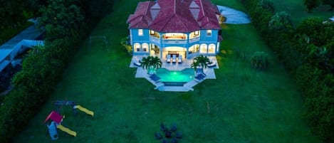A large house with a swimming pool, surrounded by a well-maintained lawn and trees.