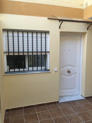 A room with a window with metal bars, a white door, and brown tiled flooring. - WONDERFUL APARTMENT IN FUENTEBRAVIA BEACH (El Puerto de Santa María)
