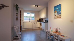 A modern kitchen with white cabinets, a sink, and a window. There is a dining area with a table and chairs, and a painting on the wall. - Beach Villa With Sauna in Makkum (Makkum)