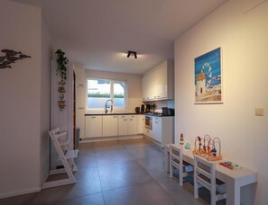 Eine moderne Küche mit weißen Schränken, einem Spülbecken und einem Fenster. Es gibt eine Essecke mit Tisch und Stühlen, sowie ein Bild an der Wand.