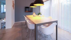 A modern dining area with a wooden table, white chairs, pendant lighting, and a large window with sheer curtains. - Beach Villa With Sauna in Makkum (Makkum)