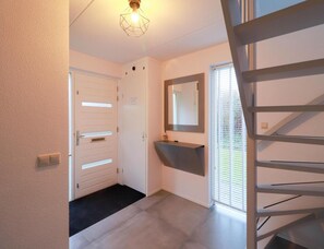 Un couloir avec une porte blanche, un paillasson noir, un miroir et un escalier.