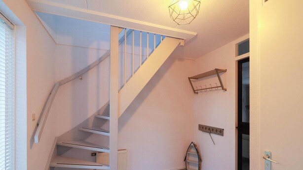 A staircase with white railings and a light fixture above it. There is a radiator on the wall and a door with a handle. - Beach Villa With Sauna in Makkum (Makkum)
