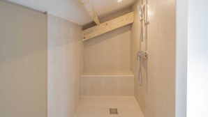 Ducha con techo de vigas de madera, cabezal de ducha de mano y panel de control en la pared.