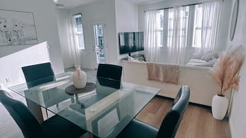 Een moderne woonkamer met een glazen eettafel, een bank en een televisie.
