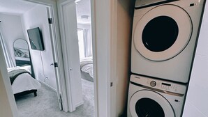 Un lavadero con dos lavadoras apiladas, una puerta que da a un dormitorio y un televisor montado en la pared.