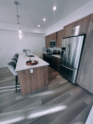 A modern kitchen with a central island, stainless steel appliances, and wooden cabinetry. - Fully equipped townhouse with a garage, 14 minutes from YYC Airport. Wi-Fi. (Airdrie)