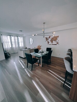 A modern living space with a dining area, a kitchen, and a large window with curtains. - Fully equipped townhouse with a garage, 14 minutes from YYC Airport. Wi-Fi. (Airdrie)