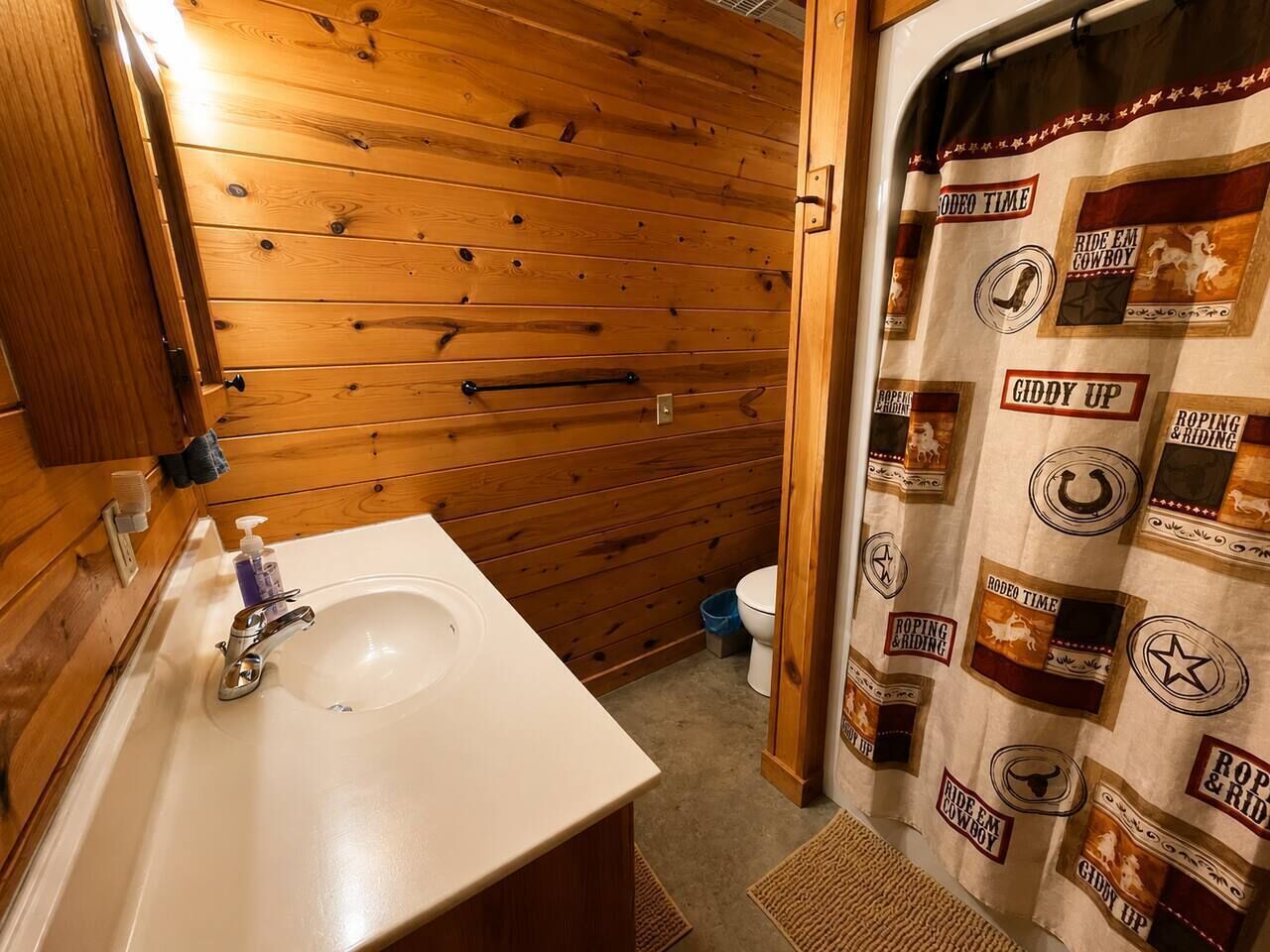 A bathroom with a wooden wall, a white sink, and a shower curtain with cowboy-themed designs.