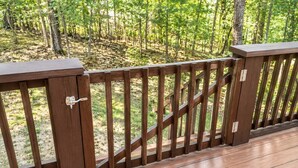 A wooden deck with a metal gate, surrounded by a forested area. - Arrowhead Ridge 3 bedroom 3 bathroom, hot tub, wrap around deck. (Broken Bow)