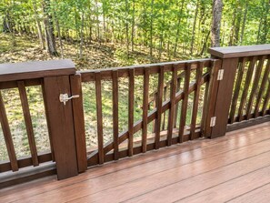 Eine Holzterrasse mit einem Metallzaun, umgeben von bewaldetem Gebiet.
