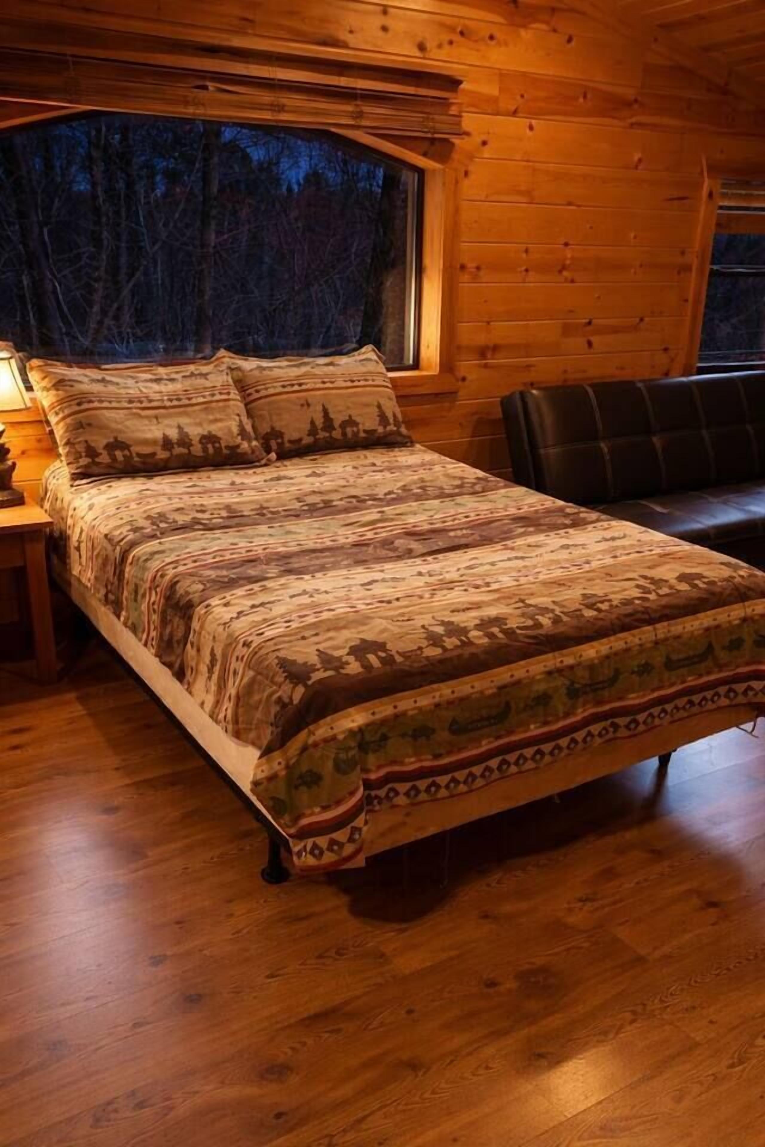 A wooden cabin bedroom with a bed, a window, and a nightstand.