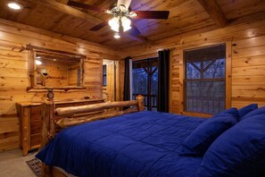 Een slaapkamer in een blokhut met een bed, een houten dressoir, een spiegel en een plafondventilator.