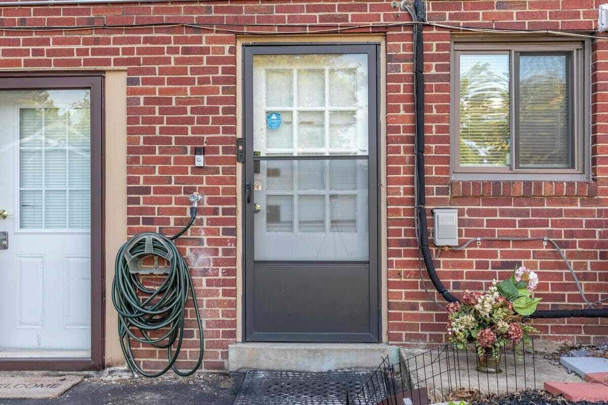 A brick building with a front door, a window, and a hose coiled against the wall.