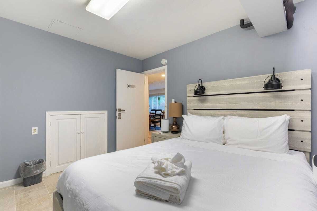 Een hotelkamer met een bed, nachtkastje, lamp en een deur die naar een andere kamer leidt.