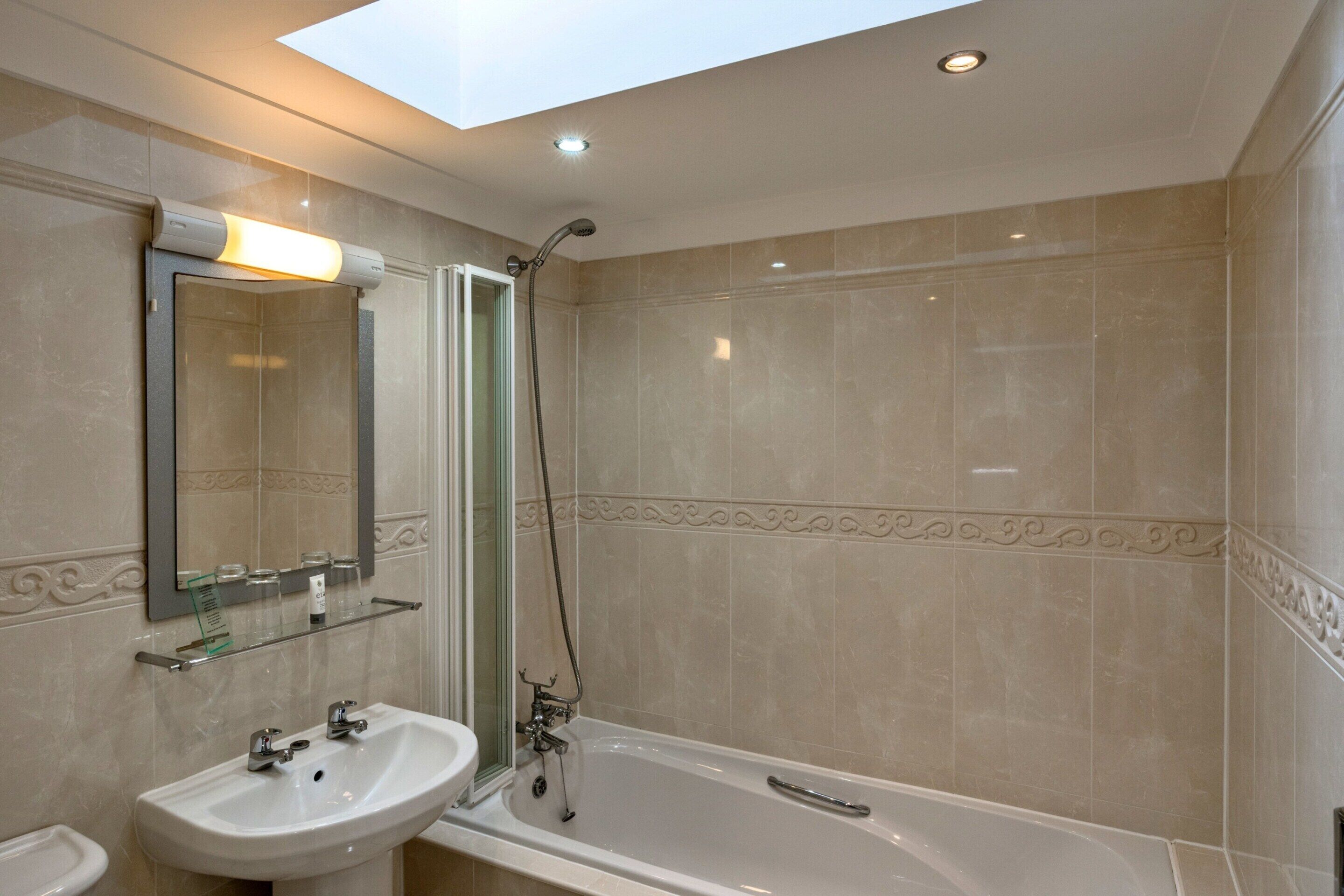 Une salle de bain avec un puits de lumière, une baignoire, un lavabo et une douche.