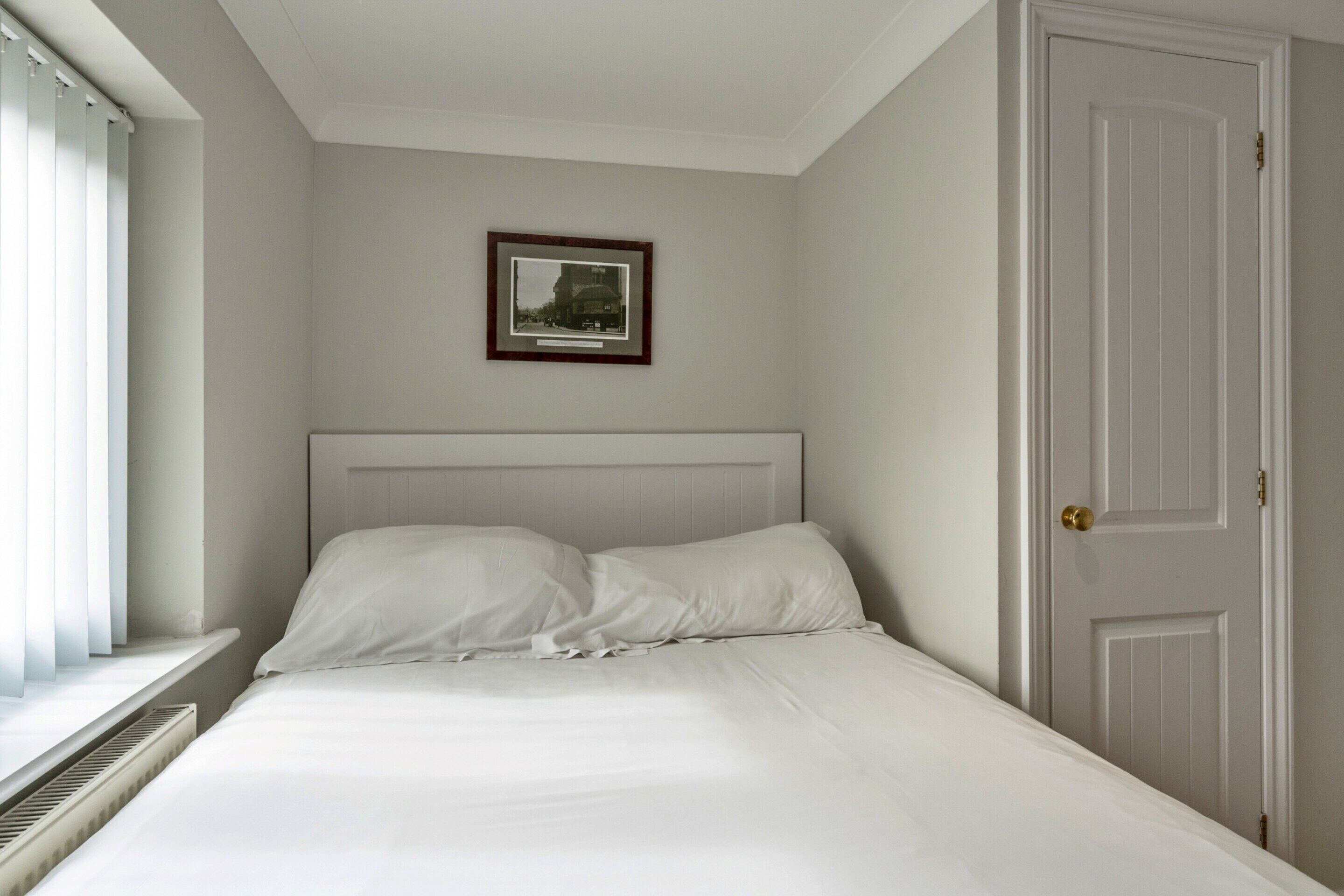 A bedroom with a bed, a framed picture on the wall, and a door.
