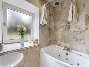 A bathroom with a bathtub, a shower, a window with a vase of flowers, and towels. - Barn Cottage With Hot Tub (Colintraive)