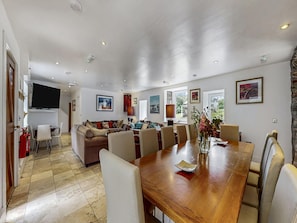 A spacious living area with a large wooden dining table, comfortable seating, a flat-screen TV mounted on the wall, and artwork on the walls. - Barn Cottage With Hot Tub (Colintraive)