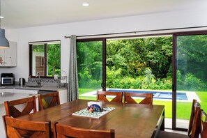 A modern kitchen with a built-in oven, a sink, and a window overlooking a lush garden and pool.
