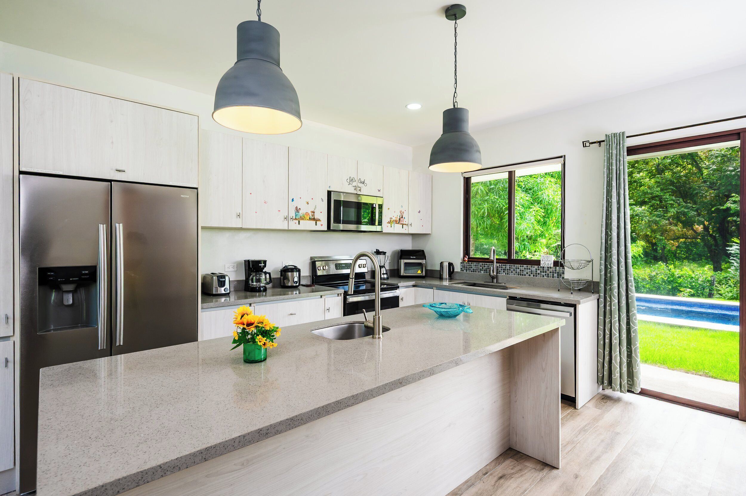 Een moderne keuken met roestvrijstalen apparatuur, een centraal eiland en hangende lampen.