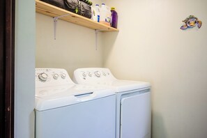 Un espace buanderie avec un lave-linge et un sèche-linge blancs, une étagère au-dessus contenant des produits de nettoyage, et un autocollant mural représentant une tortue.