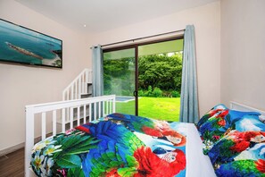 A bedroom with a bed, a window, and a view of a garden.