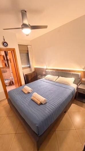 A bedroom with a bed, a ceiling fan, a nightstand, and a window with curtains. - AmdarVillage Cozy Garden Apt. (Eilat)