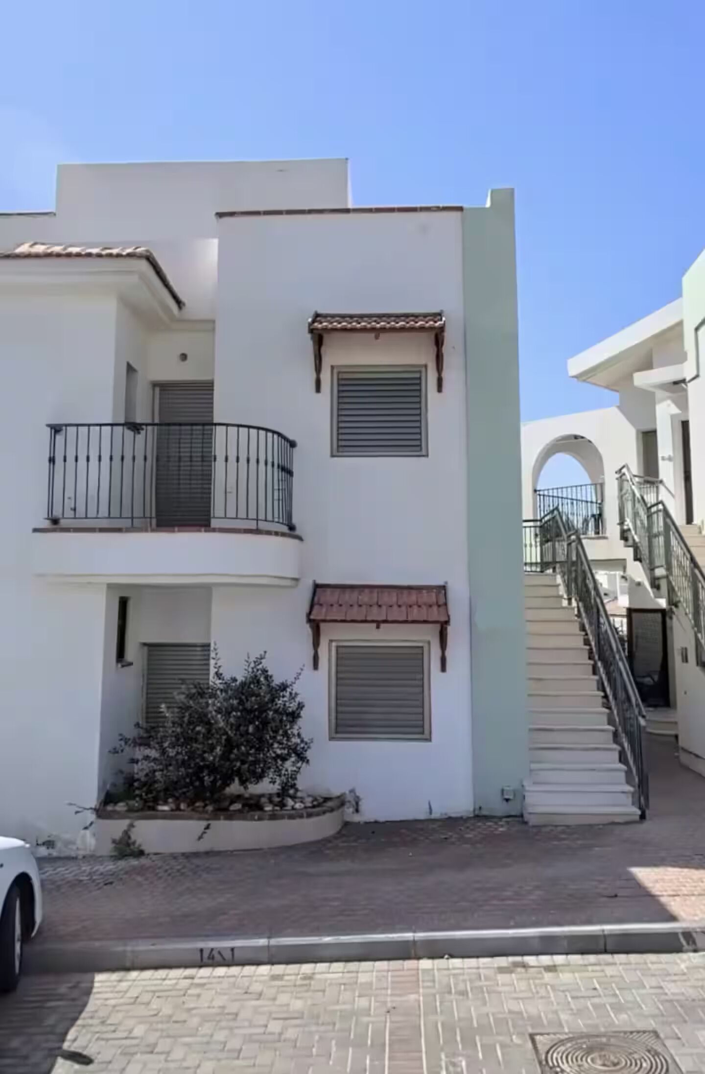 Un immeuble résidentiel à plusieurs étages, doté de balcons, d’un escalier et d’un petit jardin.