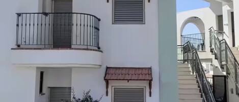 Um edifício residencial de vários andares com varandas, uma escadaria e um pequeno jardim.