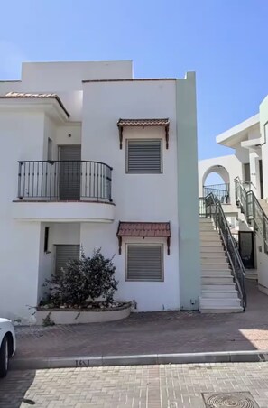 Un immeuble résidentiel à plusieurs étages, doté de balcons, d’un escalier et d’un petit jardin.