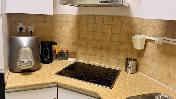 A kitchen with a stainless steel range hood, a coffee maker, a kettle, and a spice rack. - AmdarVillage Cozy Garden Apt. (Eilat)