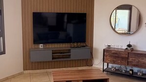 A living room with a flat-screen TV, a ceiling fan, a wooden cabinet, and a sofa. - AmdarVillage Cozy Garden Apt. (Eilat)
