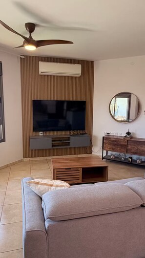 A living room with a flat-screen TV, a ceiling fan, a wooden cabinet, and a sofa. - AmdarVillage Cozy Garden Apt. (Eilat)
